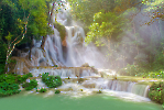 A serene turquoise pool at Kuang Si Waterfalls surrounded by lush green foliage.