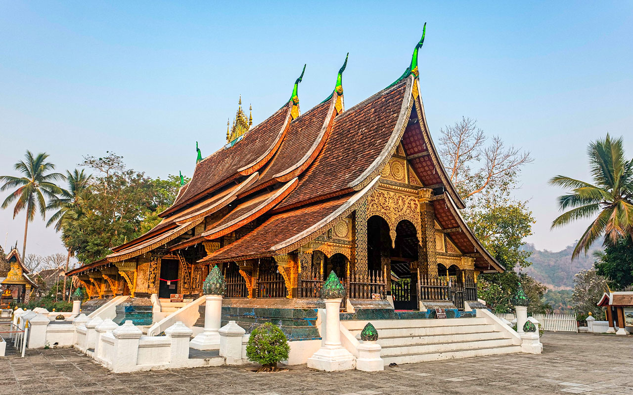 The ornate roof of Wat Xieng Thong temple in Luang Prabang, Laos, silhouetted against a vibrant sclear sky.