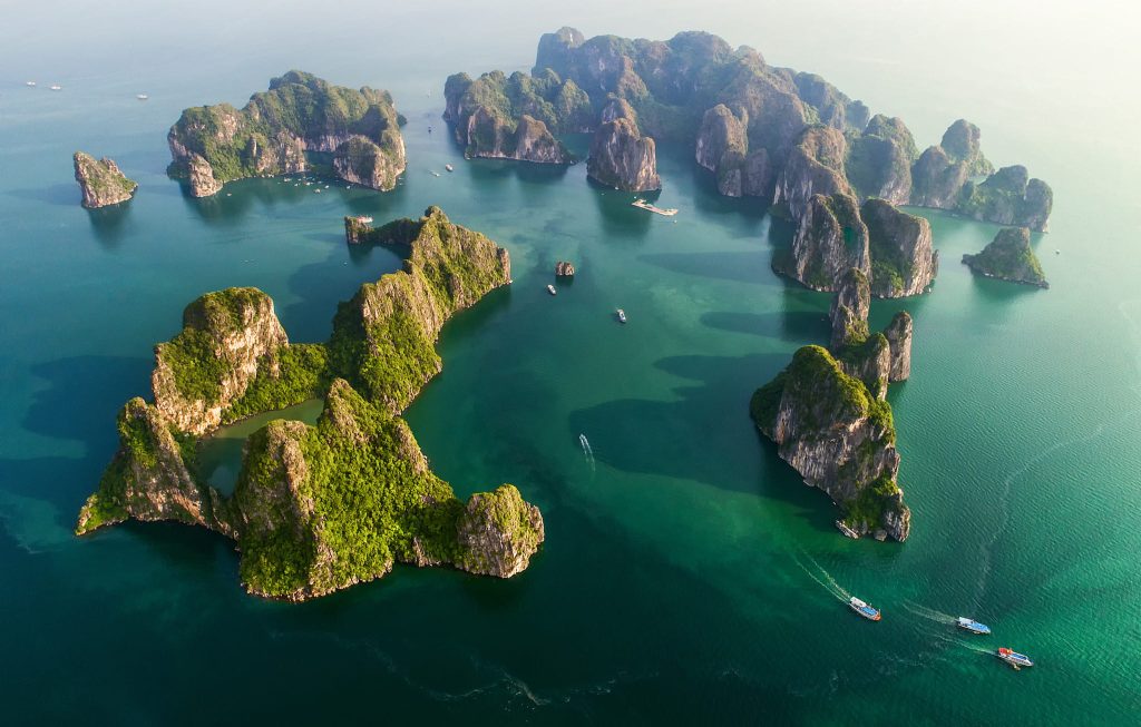 Halong Bay in Northern Vietnam with towering limestone pillars jutting out of emerald green water.