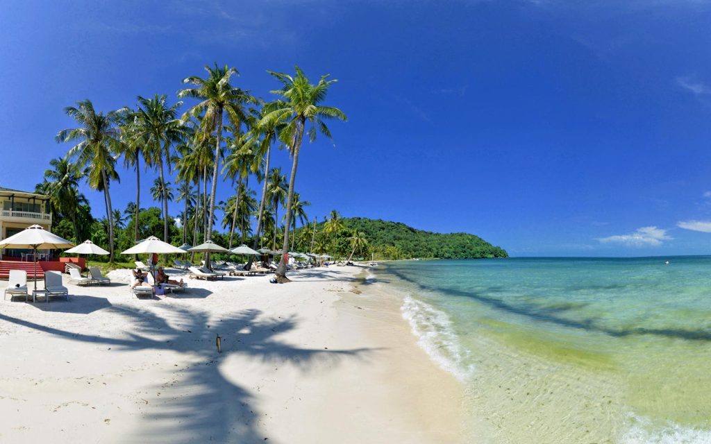 Pristine white sand beach with turquoise water and palm trees swaying in the breeze on Phu Quoc Island in Southern Vietnam.