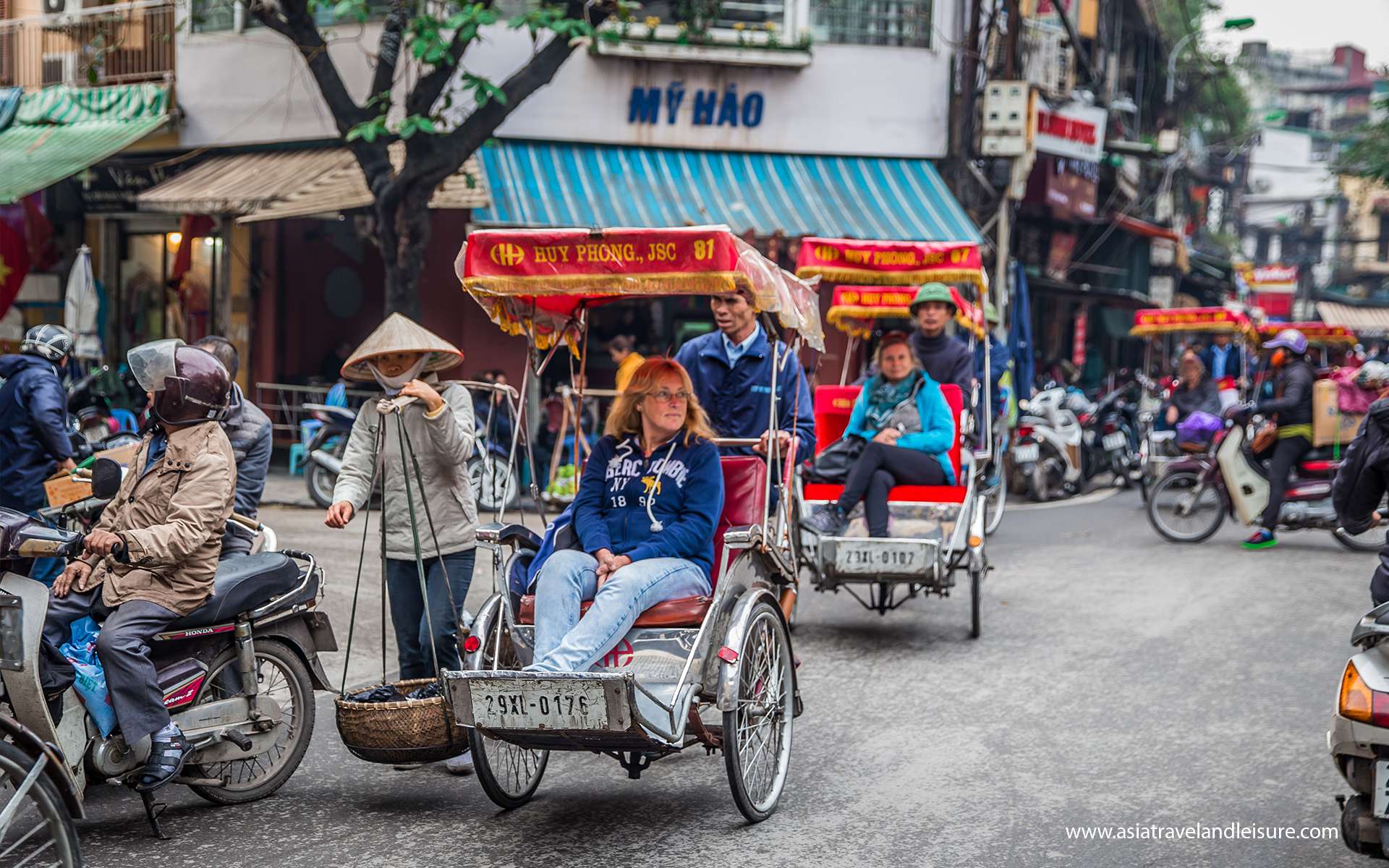 Tourists riding cyclos through Hanoi's Old Quarter amid motorbike traffic